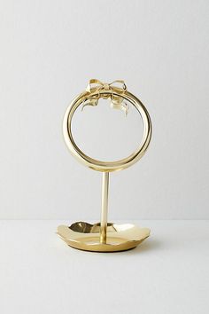 a gold ring with a bow on it is sitting on a metal stand against a white wall