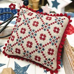 a red, white and blue pillow sitting on top of a wooden table next to scissors