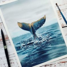 a watercolor painting of a whale's tail in the ocean with paintbrushes next to it