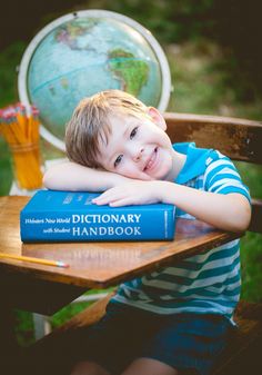 a young boy sitting at a table with two books on top of it and a globe in the background