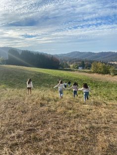 four girls are holding hands and running in a field on a sunny day with the sun shining down