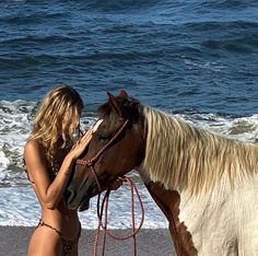 a woman standing next to a brown and white horse on top of a sandy beach