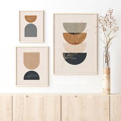 three framed art pieces hang on the wall above a wooden cabinet with a plant in it