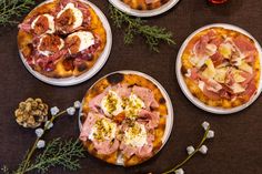 four small pizzas with different toppings sitting on a table next to some flowers