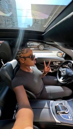 a woman sitting in the driver's seat of a car with her hand up