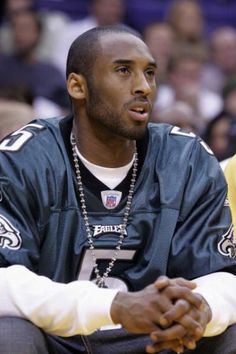 a close up of a person sitting on a bench wearing a jersey and chain necklace