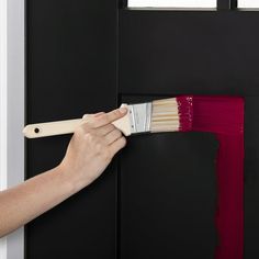 a person holding a paint brush in front of a black door with red and white stripes