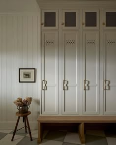 a room with white cupboards and a wooden bench in front of the cabinet doors