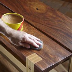 a person with a brush on top of a wooden table next to a yellow cup