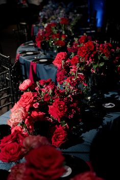 a long table is covered with red flowers and black linens for an elegant dinner