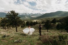 a man and woman standing in the middle of a field with mountains in the background