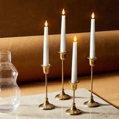 three white candles are sitting on a table next to a vase and some glassware