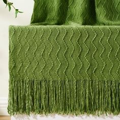 a green blanket sitting on top of a wooden floor next to a potted plant