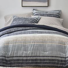 a bed with blue and white striped comforter next to a painting on the wall