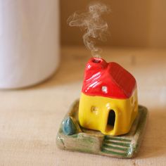 a small toy house sitting on top of a wooden table next to a white cup