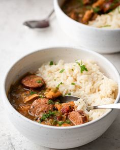 two white bowls filled with rice and sausage stew next to each other on a table