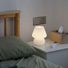 a white lamp sitting on top of a bed next to a box and pillow in a room