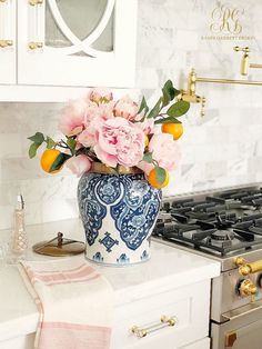 a blue and white vase filled with pink flowers on top of a counter next to an oven