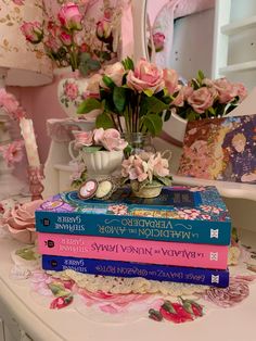 a stack of books sitting on top of a table next to a vase filled with flowers