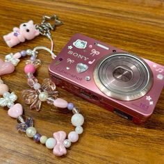 a pink camera sitting on top of a wooden table next to some beads and charms