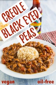 a white plate topped with beans and rice next to a bottle of chili sauce on a table