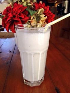 a glass filled with milk sitting on top of a wooden table next to a red flower