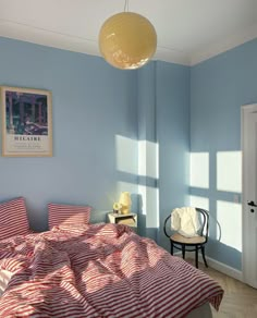 a bedroom with blue walls and striped bedspread on the bed is lit by a yellow lamp