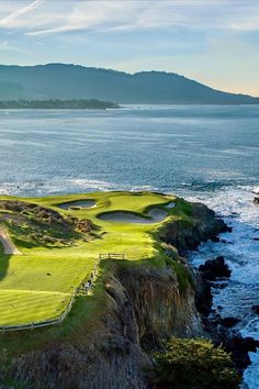 a golf course near the ocean with mountains in the background