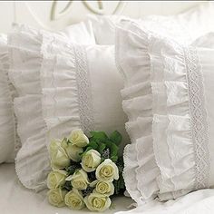 some white roses are laying on the bed with ruffles and pillows in front of them