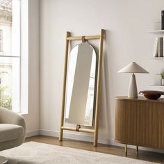 a large mirror sitting on top of a wooden stand in a living room next to a window