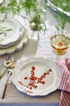 the table is set with plates, silverware and green plants in vases on it