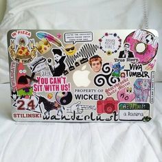 an apple laptop covered in stickers on a bed