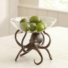 a glass bowl filled with green fruit sitting on top of a wooden table next to a window