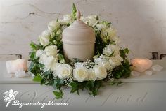 a candle surrounded by white flowers and greenery on a mantle with candles in the background