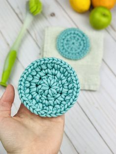 a hand holding a crochet dishcloth in front of some fruit