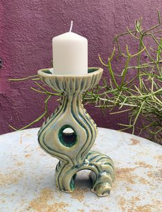 a candle holder sitting on top of a table next to a plant and purple wall