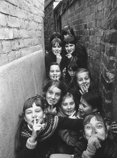 black and white photograph of children with faces painted on their mouths, standing in front of a brick wall