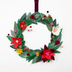 a christmas wreath made out of felt with flowers and leaves hanging from the side on a white wall