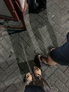 two people standing next to each other on a brick sidewalk with their feet propped up