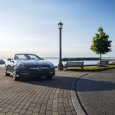 a car parked on the side of a road near a light pole and bench with water in the background