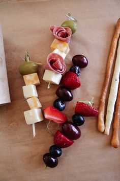 an assortment of fruits and cheeses are arranged on a cutting board next to breadsticks