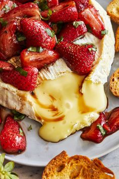 a white plate topped with strawberries covered in cheese and sauce next to bread slices