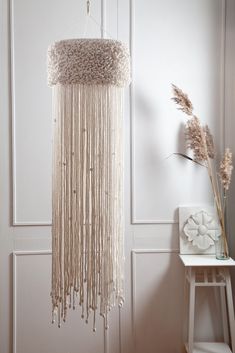 a white wall hanging with beads on it next to a table and vase filled with flowers