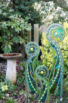 a garden sculpture made out of glass in the middle of some grass and flowers next to a birdbath