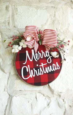 a merry christmas sign hanging on the side of a stone wall with red and white bows