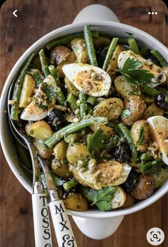 a bowl filled with green beans, potatoes and an egg on top of a wooden table