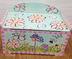 a painted wooden toy box with flowers and butterflies on the lid, sitting on a wood floor