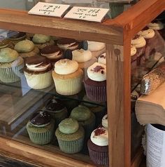 a display case filled with lots of different types of cupcakes on top of wooden shelves