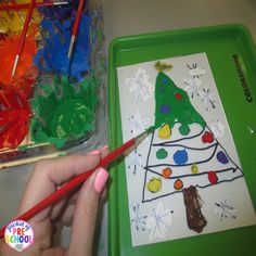 a child's hand is holding a pencil and drawing a christmas tree on paper