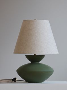 a green lamp sitting on top of a table next to a white wall and a beige shade